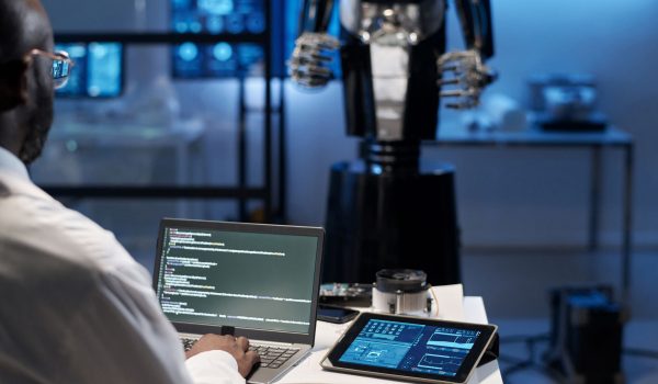 Een robot en een man die codes op een laptop typt