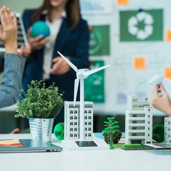 Kantooromgeving met op de achtergrond mensen die iets bespreken en op de voorgrond een stad in het klein, met groene omgeving en een windmolen